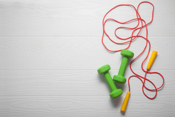 dumbbells with skipping rope on white wooden surface, copy-space left