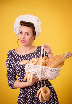 A girl dressed as a chef holding a basket of bread isolated on yellow background