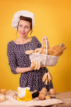 A girl dressed as a chef holding a basket of bread on yellow isolated background