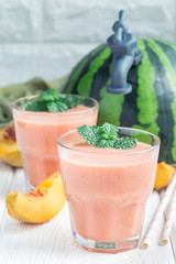 Watermelon, peach, mint and coconut milk smoothie in glass on white wooden background, vertical