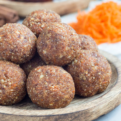 Obraz na płótnie Canvas Homemade paleo energy balls with carrot, nuts, dates and coconut flakes, on wooden plate, square format