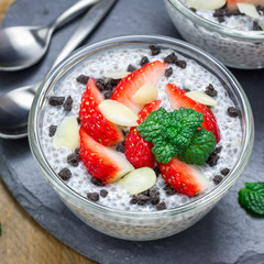 Chia seed pudding with strawberries, almond and chocolate cookie crumbs, on slate board, square format