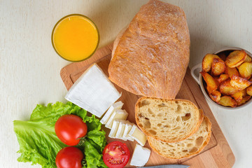 Breakfast from bread, cheese, tomatoes, potatoes and all-over salad on a wooden table closeup.
