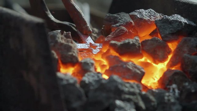 In the smithy the metal cross is heated on coals in the furnace