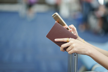close up woman hand holding passport and playing smartphone on her suitcase at airport while waiting for boarding time ,traveler concept