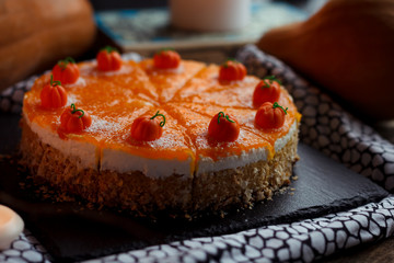 Traditional american fresh round bright orange tasty homemade pumpkin pie on decorative table with textil, pumpkins and candles light. Dark food photo concept
