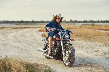 Stylish young woman posing on a motorcycle in the countryside .