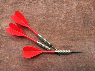 Three red darts on the wood floor.  For sport, dart is an indoor game with plastic flights are...
