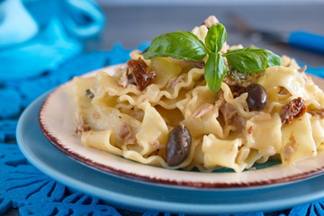 Pasta with olives, tuna, sun dried tomatoes and olive oil in a white and blue plate on a blue cloth.