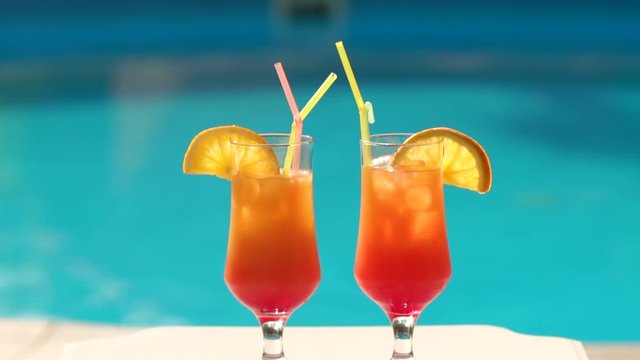 Close-up of two orange cocktail with orange slices and ice in the background of the pool.