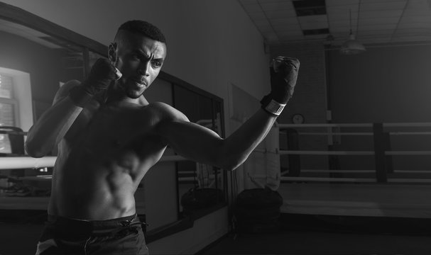 Afro american male boxer. Young man boxing workout in a fitness club. Muscular strong man on background boxing gym. Black and white photo.
