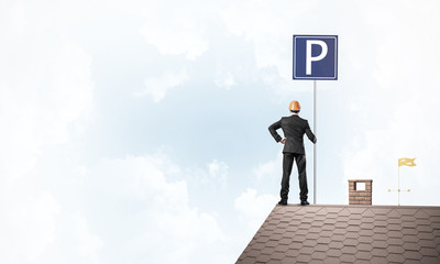 Young businessman with parking sign standing on brick roof. Mixe