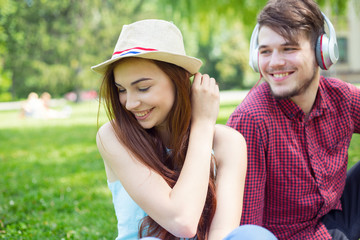 Portrait of a girl sitting next to the guy. Happy couple of young people having fun together on the green grass in the park campus.