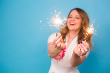 Portrait of a happy woman holding bengal lights over blue background with copy space. Christmas, celebrations and holidays concept
