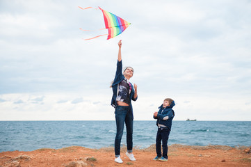 happy mother and little child wearing autumn clothes playing kite on storm sea background