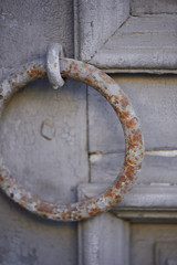 Old vintage grey door with peeling paint and a rusty handle in the form of a ring
