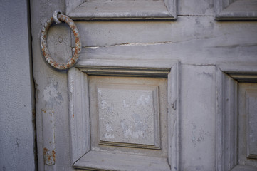 Old vintage grey door with peeling paint and a rusty handle in the form of a ring