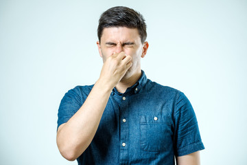 Man holding his nose against a bad smell over gray background