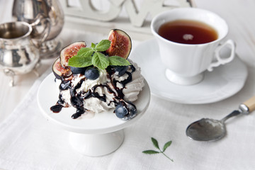 A cup of tea and a meringue cake decorated with blueberries and figs on a white wooden background. Selective focus, close-up.
