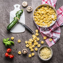 Tortellini with zucchini and vegetarian cooking ingredients on kitchen table background with cutting board and knife, top view. Healthy cooking and eating. Italian food concept