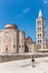 Blond girl is photographing monuments of historic center of the Croatian town of Zadar at the Mediterranean Sea, Europe.