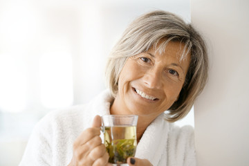 Senior woman in bathrobe drinking hot green tea