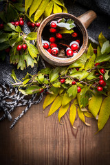 Cup of healthy tea with scarf, autumn leaves and berries on rustic wooden background.  Hot autumn beverages concept, top view, place for text,vertical