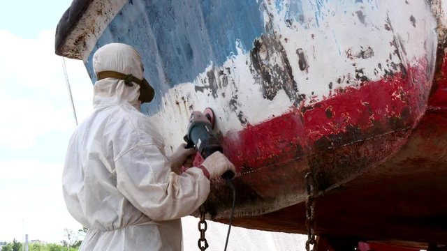 Working people tear off paint on metal in repairs process at shipyard. Workers in overalls reconstruct at ship repair yard outdoors in port.