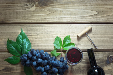 Open bottle of red wine with a glass, corkscrew and ripe grape on a wooden board. Copy space and top view.