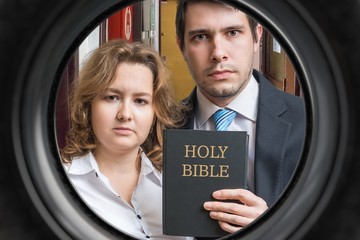 Jehovah witnesses are showing bible behind door. View from peephole.