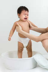 Portrait of a crying baby sitting in the basin for shower, indoors