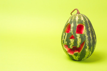 Watermelon with a smiling face like a pumpkin for Halloween. Green background with empty space for text