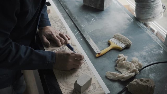 Worker traces lines with a stencil handle, the pattern is transferred to a marble slab using a carbon paper, a workplace, a sketch is drawn on lined paper