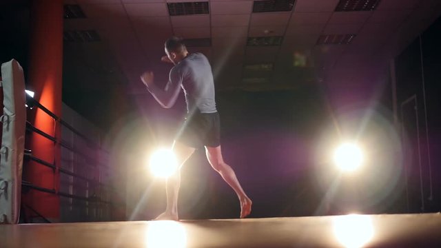 A boxer trains on an empty gym floor under spotlights.