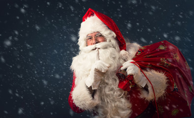 Santa Claus making a silence gesture, on dark background 