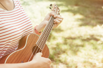 Anonymous woman playing on ukulele in the summer park