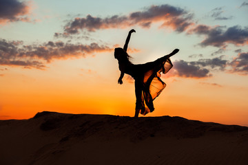 Dancing at night in the sand against the backdrop of the setting sun, the silhouette of a dancer.