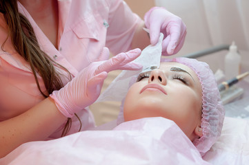 A young woman lies and gets a make-up of her eyebrows in a beauty salon. The use of permanent...