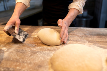 baker portioning dough with bench cutter at bakery