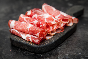 Parma ham or Hamon on a wooden cutting board. Dark background.