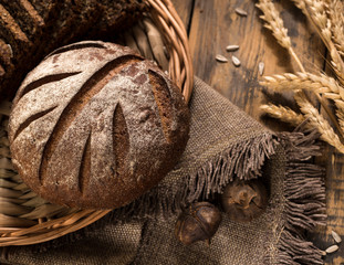 Fototapeta na wymiar round rye bread in a wicker tray with a napkin and spikelets on wooden surface