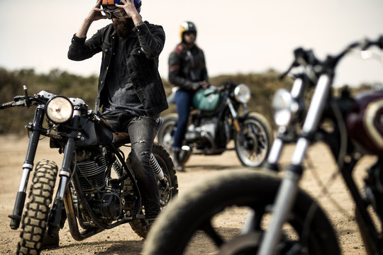 Three men sitting on cafe racer motorcycles on dirt road