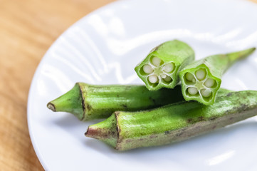 Fresh okra in white dish on wooden table.