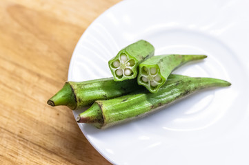 Fresh okra in white dish on wooden table.