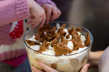 child and mother sprinkle biscuit over an authentic homemade family christmas gingerbread custard trifle