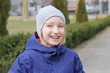 Cheerful preteen girl 9-11 year old laughing on a walk outdoors. Wearing warm jacket and hat.