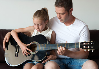 Dad teaches daughter to play guitar.