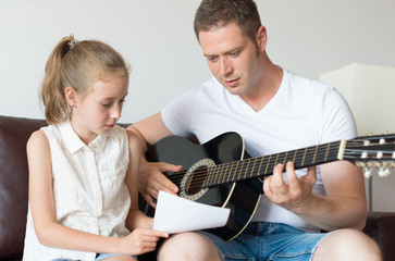 Dad and his daughter compose a song on the guitar.