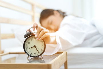 Young asian woman press the button snooze wake up alarm clock alert in the morning and sleeping...