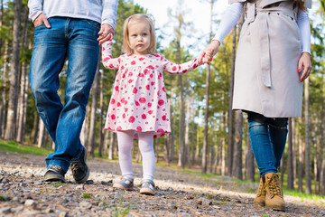 Happy young family taking a walk in a park, family holding hands walking together along forrest path